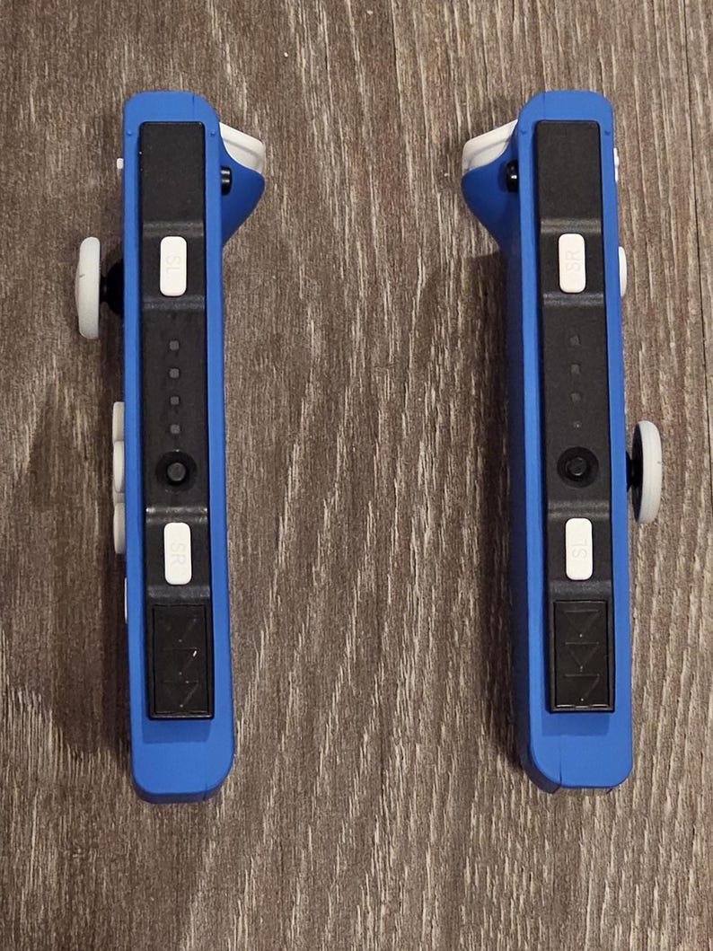 May include: Two blue Nintendo Switch Joy-Con controllers with black buttons and white accents. The controllers are in a vertical position and have a black and white design.