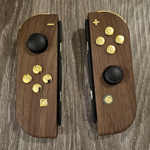May include: Two brown wooden game controllers with gold-colored buttons and accents. Each controller has a black joystick and a set of buttons. The controllers are designed for a gaming console.