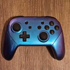 May include: A blue and purple iridescent Nintendo Switch controller with black buttons and a black d-pad.