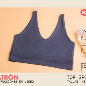 Puede incluir: Un patrón de costura PDF para un top deportivo azul oscuro. El patrón incluye instrucciones en formato de video. El patrón está disponible en tallas XS-XXL. El texto "PATRÓN INSTRUCCIONES EN VIDEO" y "TOP SPORT TALLAS: XS-XXL" es visible en la imagen.