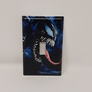 Könnte beinhalten: Ein Lichtschalter-Abdeckung mit einer Nahaufnahme von Venoms Gesicht mit einer roten Zunge und einem dunkelblauen und schwarzen Hintergrund.