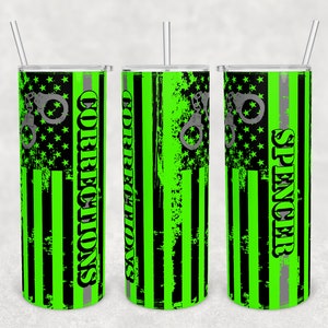 May include: Three green and black stainless steel tumblers with a distressed American flag design. The tumblers have a silver lid and a silver straw. The text "Corrections" is on one tumbler, the text "Spencer" is on another tumbler, and the third tumbler has a handcuff design.