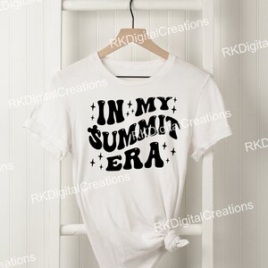 May include: White t-shirt with black text that reads "IN MY SUMMIT ERA" with stars around the text.
