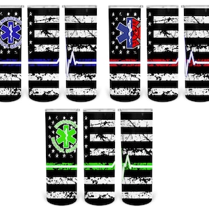 May include: Set of six black and white tumbler cups with a distressed American flag design. Each cup features a different color stripe across the bottom and a symbol representing emergency services: a blue stripe with a medical star, a red stripe with a fire department symbol, a green stripe with a medical star, a blue stripe with a heartbeat, a red stripe with a heartbeat, and a green stripe with a heartbeat.