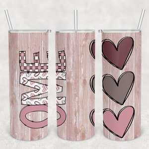 May include: Three stainless steel tumblers with a wood grain pattern and different designs. The first tumbler has the word "LOVE" in pink with a plaid and heart pattern. The second tumbler has a wood grain pattern. The third tumbler has three hearts in shades of pink and brown.