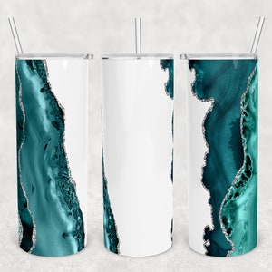 May include: Three stainless steel tumblers with a teal and silver agate design. The tumblers are white with a teal and silver agate design on one side. The tumblers are on a gray background.
