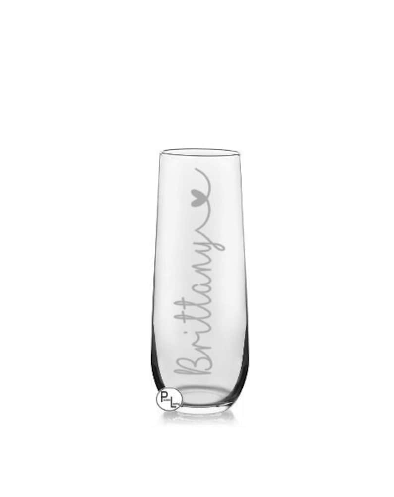May include: A clear glass champagne flute with the name "Brittany" etched on the side, with a small heart above the name.
