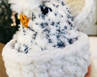 Puede incluir: Un juguete de pollo de peluche hecho a mano con una cabeza blanca y esponjosa y un cuerpo salpicado de azul oscuro. El pollo está metido en una cesta blanca suave y texturizada. El pico es amarillo y el ojo es negro.