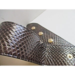 May include: Close-up of a pair of brown snakeskin-patterned shoes. The shoes have a pointed toe and are embellished with gold-colored studs. The texture of the snakeskin is visible, with a glossy finish.