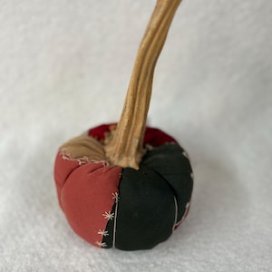 Può includere: Una zucca di stoffa fatta a mano con un gambo marrone. La zucca è composta da pannelli di tessuto cuciti in rosso, nero e marrone, con cuciture bianche a forma di stella. Un accessorio decorativo autunnale per la casa.