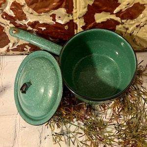 May include: A vintage green enamelware saucepan with a lid. The saucepan has a speckled green finish and a black rim. The lid has a small handle.