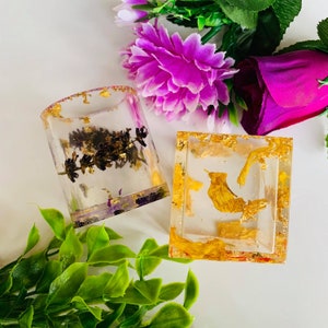 May include: Two clear resin containers with gold leaf and dried flowers. One container is cylindrical and the other is square.