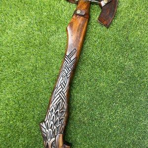 Puede incluir: Un mango de hacha de madera tallada a mano con un diseño de lobo detallado. La cabeza del hacha es de metal y tiene una funda de cuero.