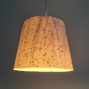 May include: A light brown lampshade with a delicate pattern of black lines. The lampshade is hanging from a white cord.