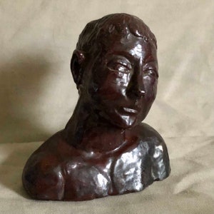 May include: A dark brown ceramic bust sculpture of a person with a short haircut. The sculpture is detailed with facial features and a textured surface.