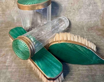 May include: A set of four vintage green and gold enamel and glass brushes. The set includes a tall glass jar with a green lid, a long glass tube with a green lid, and two smaller brushes with green and gold handles.