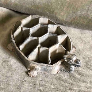 May include: A grey ceramic turtle trinket box with a hexagonal design on the top. The turtle has a detailed head and legs.