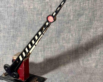 Könnte beinhalten: Vintage Spielzeug-Eisenbahnübergangssignal. Der schwarz-weiß gestreifte Arm hat ein rot-weißes "STOP"-Schild. Der Sockel ist schwarz mit roter Stütze und Metallbasis. Ein klassisches Spielzeug.