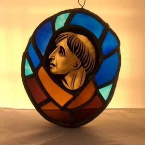 Könnte beinhalten: Ein Buntglasfenster mit dem Profil einer Person in Blau-, Braun- und Goldtönen.