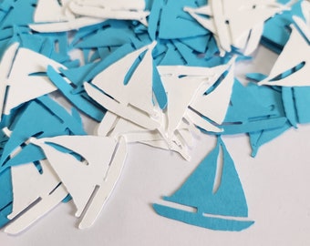 May include: A pile of blue and white paper sailboats. The sailboats are cut out of paper and are scattered on a white surface.