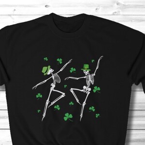 May include: Black sweatshirt with a graphic of two skeletons wearing green hats and dancing. The skeletons are surrounded by green shamrocks.
