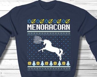 May include: A navy blue sweatshirt with a white unicorn design and the text "Menoracorn". The design features a menorah and a unicorn horn. The sweatshirt has a festive, holiday-themed pattern.