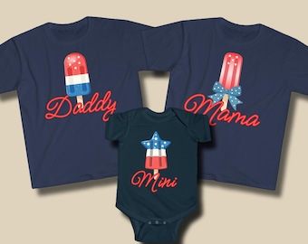 May include: Navy blue t-shirts and a onesie with patriotic popsicle designs. The shirts say "Daddy" and "Mama" in red script, and the onesie says "Mini". The popsicle designs feature red, white, and blue colors, perfect for family matching.