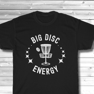Puede incluir: Camiseta negra con un gr&aacute;fico blanco de una canasta de disc golf y el texto "BIG DISC ENERGY".