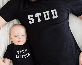 May include: A black t-shirt with the word "STUD" printed in white on the front. A baby is wearing a black onesie with the words "STUD MUFFIN" printed in white on the front.