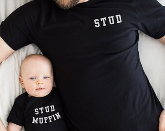 May include: A black t-shirt with the word "STUD" printed on it. A baby is wearing a black onesie with the words "STUD MUFFIN" printed on it.