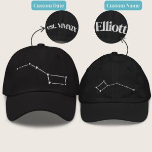 May include: Two black baseball caps with white embroidered constellation designs. One cap features the text "est. MMXIX" and the other has the name "Elliott" embroidered in white. The caps are a classic six-panel design.