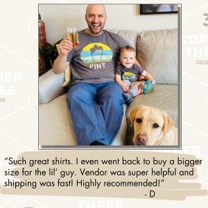 May include: A man and a child wearing matching gray t-shirts with a "PINT" design, sitting on a couch with a yellow Labrador Retriever. The man holds a glass of beer. The child holds a toy.
