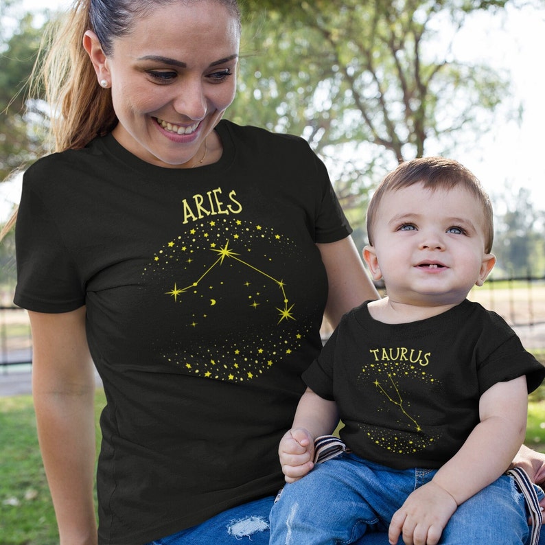 May include: A black t-shirt with a gold constellation design for Aries and a black baby t-shirt with a gold constellation design for Taurus.