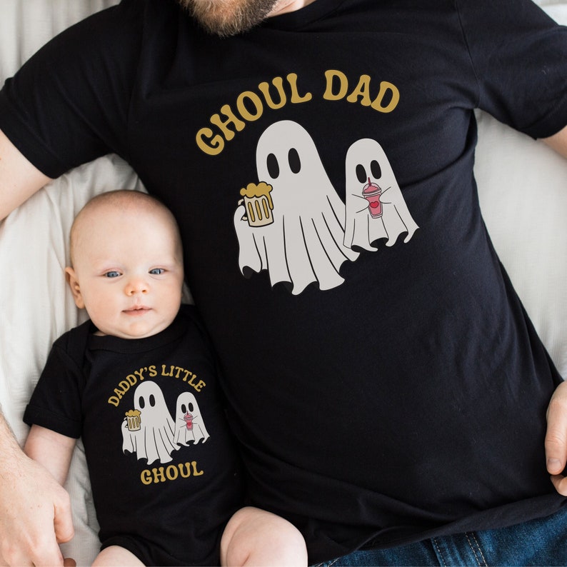 May include: A black t-shirt with the text "Ghoul Dad" and a ghost holding a beer. A black onesie with the text "Daddy's Little Ghoul" and a ghost holding a beer.