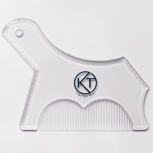 May include: A clear plastic beard shaping tool with a comb on the bottom and a guide on the top. The tool has a circle with the letters KT and the text "Valley Co." printed on it.