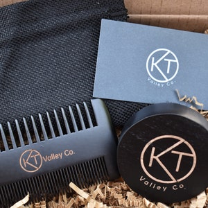 May include: A black wooden beard comb and brush set with a black drawstring bag and a business card. The comb and brush have the logo "KT Valley Co." engraved on them.
