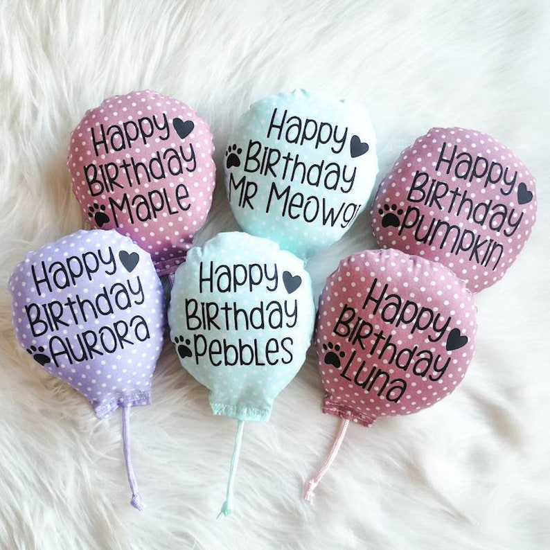 Six pink and blue polka dot fabric catnip cat toy balloons with strings. The balloons have the text 'Happy Birthday' and a paw print followed by a name: 'Maple', 'MR Meowgi', 'Pumpkin', 'Aurora', 'Pebbles', and 'Luna'.