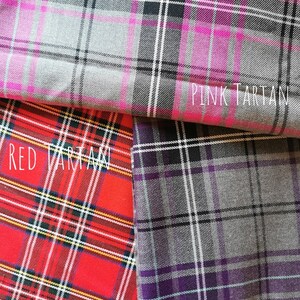 Three different tartan fabrics, one pink, one red, and one purple. The fabrics are folded over each other, with the pink fabric on top, the red fabric in the middle, and the purple fabric on the bottom. The fabrics are all patterned with a traditional tartan design.