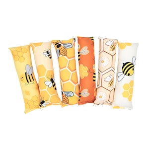 May include: A collection of six rectangular pillows with bee-themed designs. The pillows feature yellow, orange, and cream backgrounds with honeycomb patterns and cartoon bees. Some pillows have smiling bees, while others have bees with wings.