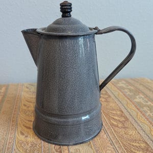May include: A gray enamel coffee pot with a black wooden knob on the lid and a black metal handle.