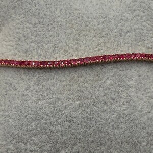 May include: A delicate gold bracelet with a row of small red gemstones.