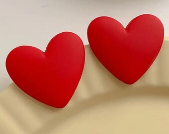 May include: Two red heart-shaped earrings. The earrings are made of a smooth, matte material.