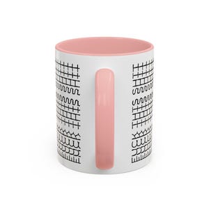 May include: White ceramic mug with a pink interior and handle. The exterior features a repeating black pattern of geometric shapes. The mug is designed for hot or cold beverages.