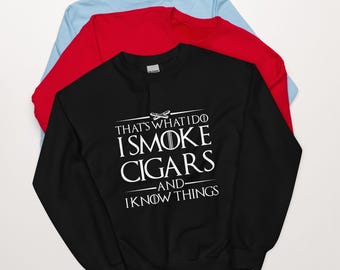 May include: Black sweatshirt with white text that reads "That's what I do I smoke cigars -and- I know things". The sweatshirt is layered on top of a red sweatshirt and a light blue sweatshirt.