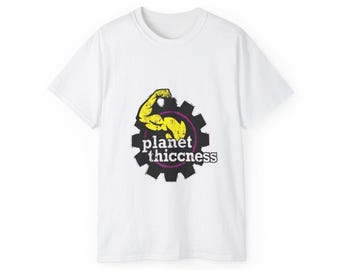 May include: A white short-sleeve t-shirt featuring a central graphic of a black gear silhouette with a yellow flexed bicep arm inside. The text "planet thiccness" is printed in white across the center of the gear, surrounded by a thin purple circle.