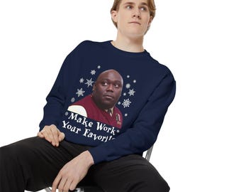 May include: Navy blue sweatshirt featuring a portrait of an individual in a maroon and white jacket, surrounded by white snowflakes. The text "Make Work Your Favorite" is printed below the portrait. The sweatshirt is worn by a person.