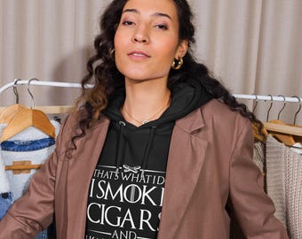 May include: A black hoodie with the text "THAT'S WHAT I'D SMOKE CIGARS -AND- I KNOW THINGS" in white. The person is wearing a brown blazer and gold hoop earrings. The hoodie has a drawstring hood and a front pocket.