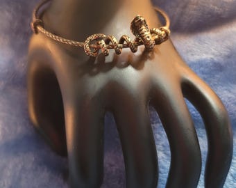 Peut inclure: Un bracelet jonc en or avec un serpent enroulé. Le serpent est texturé. Le bracelet est sur un mannequin de main noir.