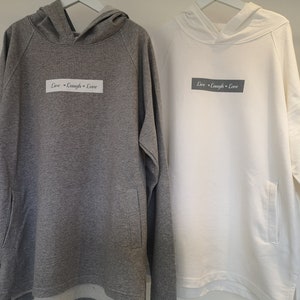 Può includere: Due felpe con cappuccio, una grigia e una bianca, con la scritta "Live - Laugh - Love" stampata sul davanti.