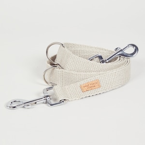 May include: A beige cotton dog lead with silver hardware and a brown leather tag that says "Snout Pouch London".